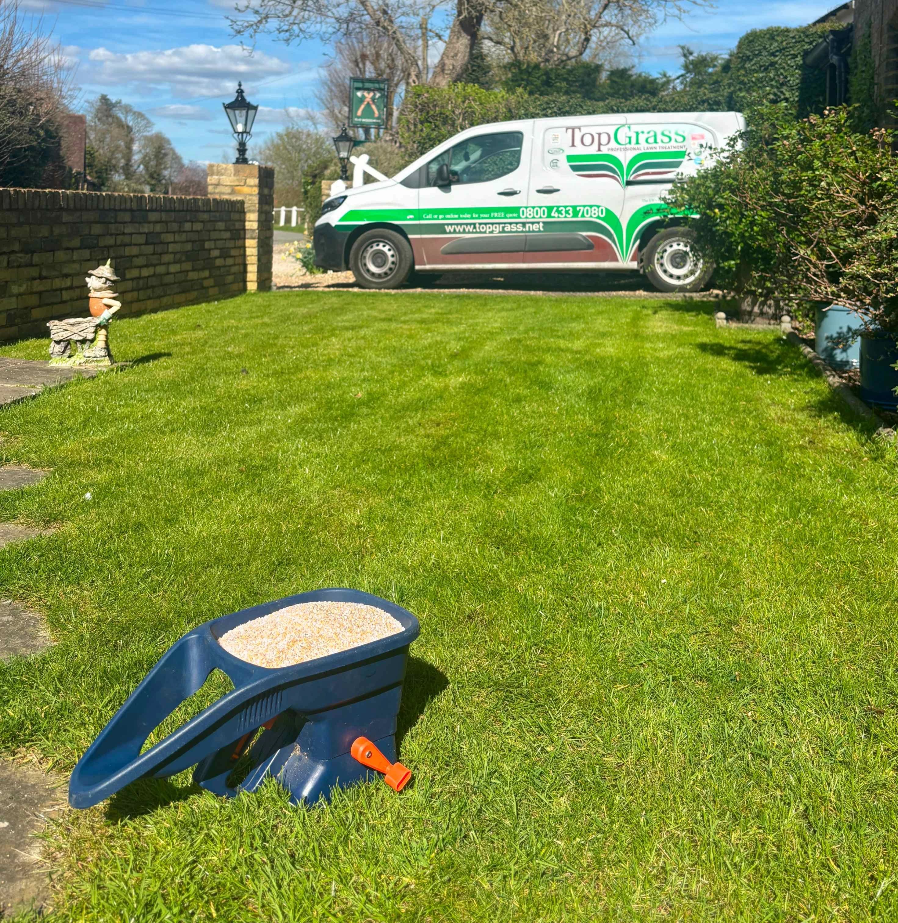 image of handheld fertliser spreader on a lawn facing a van that is branded with TopGrass